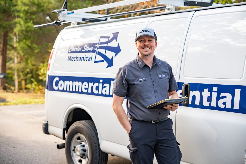 Smiling commercial and residential technician holding clipboard standing in front of business van