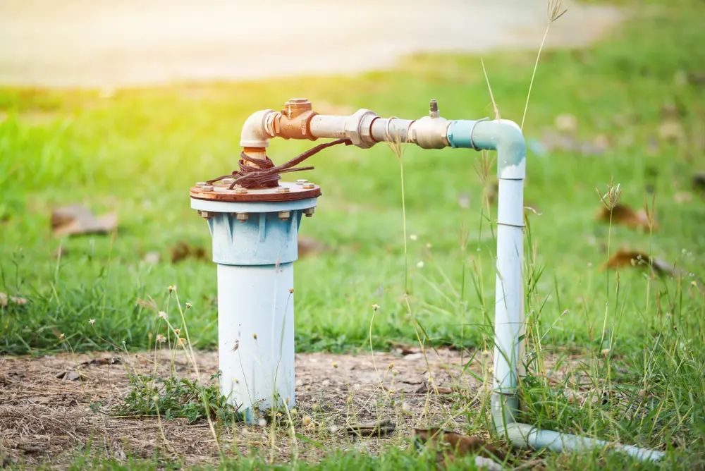 Groundwater well with pvc pipe and system electric deep well submersible pump water on green meadow