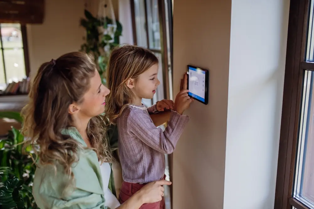 Girl helping mother to adjust, lower heating temperature on thermostat. Concept of sustainable, efficient, and smart technology in home heating and thermostats. zone control systems